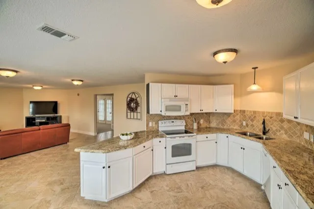 a large white kitchen with a stove top oven a sink a dining table and chairs