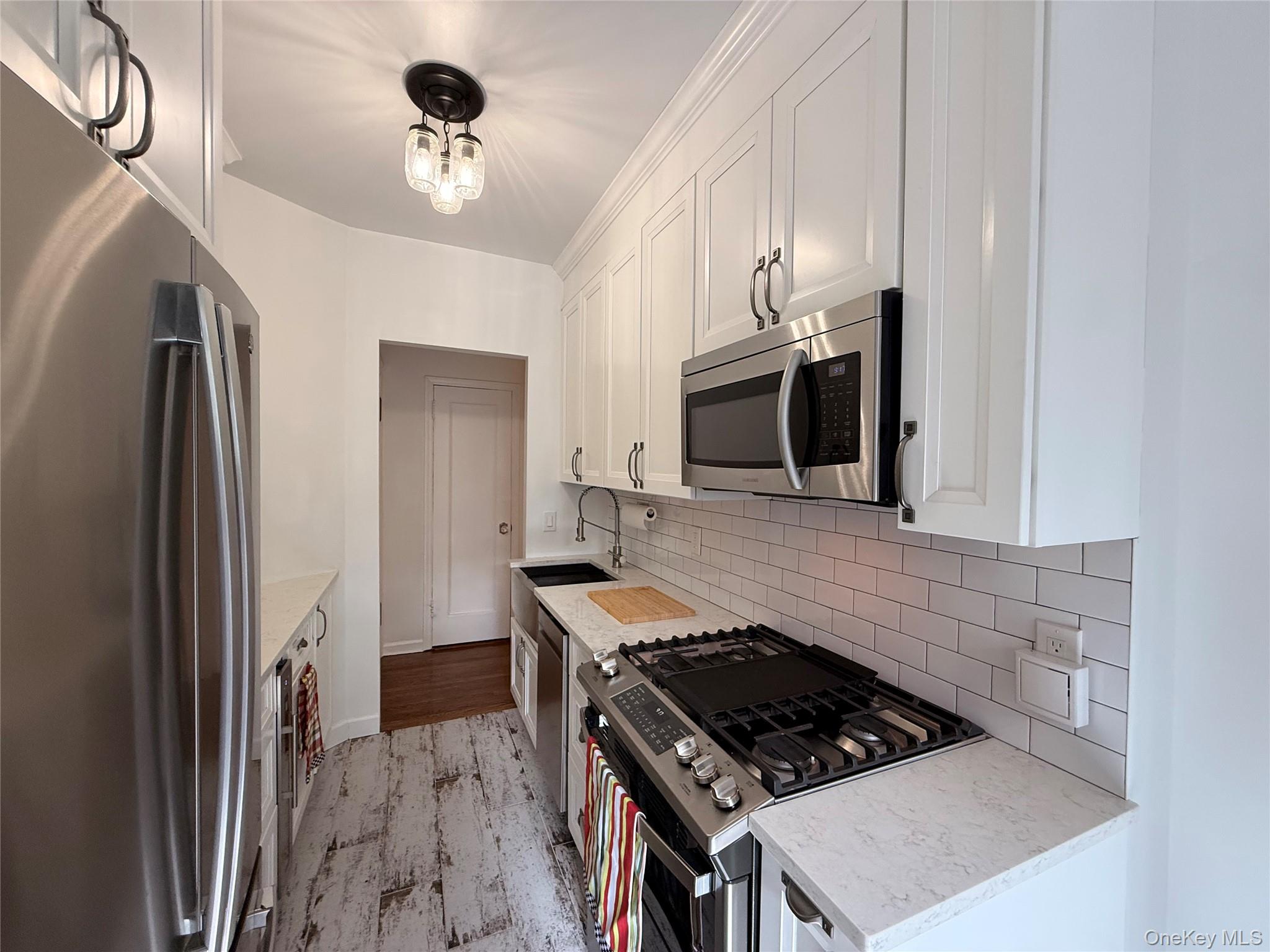 143 Garth Road, Unit 3L Scarsdale, NY 10583 - Photo 25 of 37 The kitchen features white shaker-style cabinetry, stainless steel appliances, white subway tile backsplash, and light-toned countertops