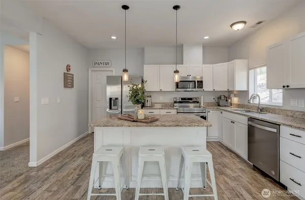 a kitchen with stainless steel appliances granite countertop a sink a stove a refrigerator and island with wooden floor