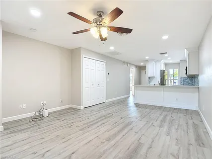 a view of an empty room and kitchen with wooden floor