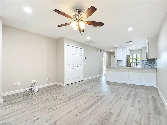 a view of an empty room and kitchen with wooden floor