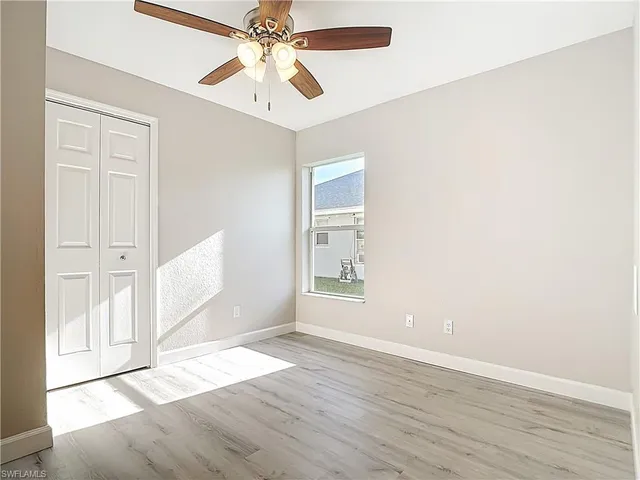 an empty room with wooden floor a ceiling fan and windows