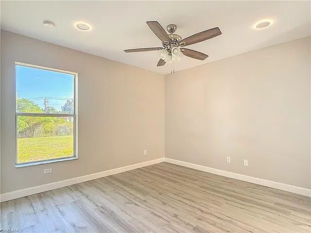 an empty room with wooden floor fan and windows