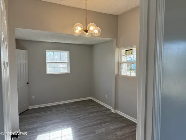 an empty room with wooden floor chandelier and windows