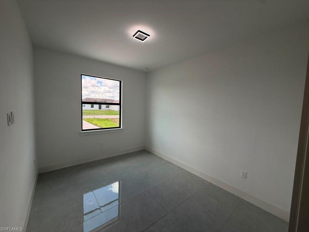 907 Homestead Road South Lehigh Acres, FL 33974 - Photo 43 of 43 Room with white walls, large window with black trim, square ceiling light fixture, and reflective grey tile flooring
