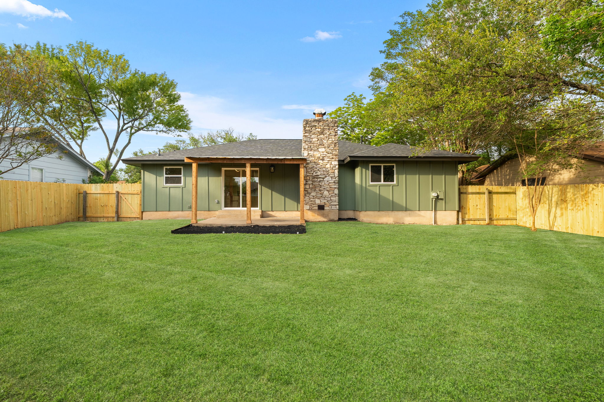 2107 Cindy Lane Austin, TX 78727 - Photo 32 of 33 Spacious backyard featuring a covered patio, extensive lawn, fencing, and stone chimney