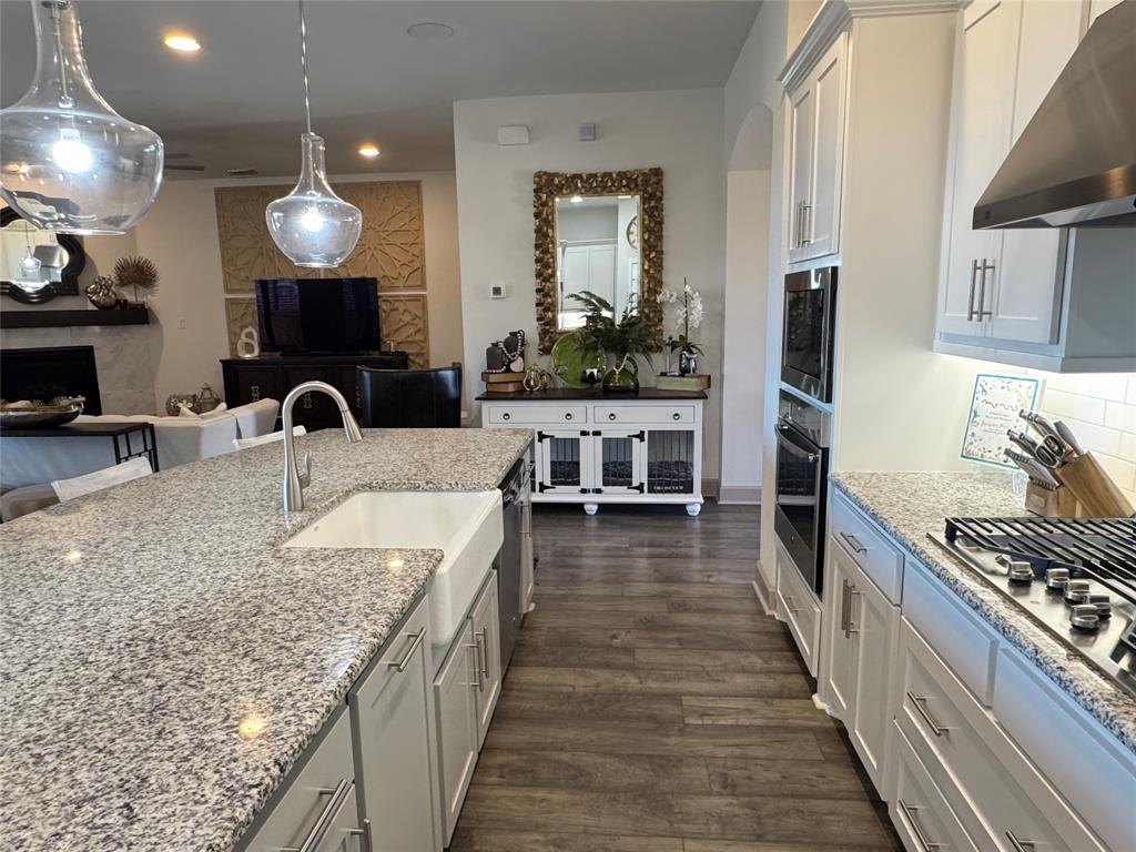 8905 Habersham Drive Rowlett, TX 75089 - Photo 29 of 31 Kitchen featuring under cabinet range hood, open floor plan, light stone countertops, decorative light fixtures, and dark wood-style floors