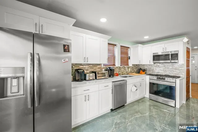 a kitchen with stainless steel appliances granite countertop a refrigerator a stove a sink and white cabinets