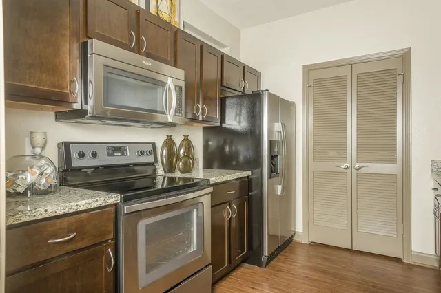 a kitchen with stainless steel appliances a stove top oven a sink a refrigerator white cabinets and wooden floor