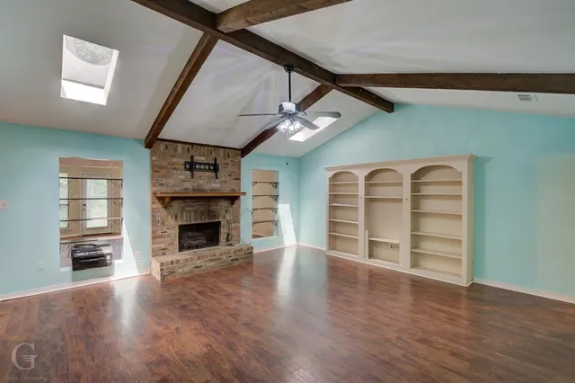 an empty room with wooden floor fireplace and windows