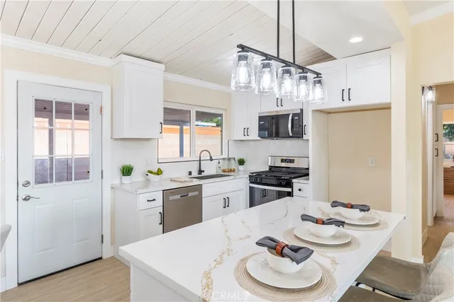 a kitchen with stainless steel appliances kitchen island granite countertop a sink dishwasher a dining table and chairs with wooden floor