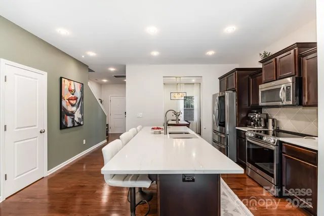 a kitchen with stainless steel appliances kitchen island granite countertop a refrigerator a stove and a sink with wooden floor