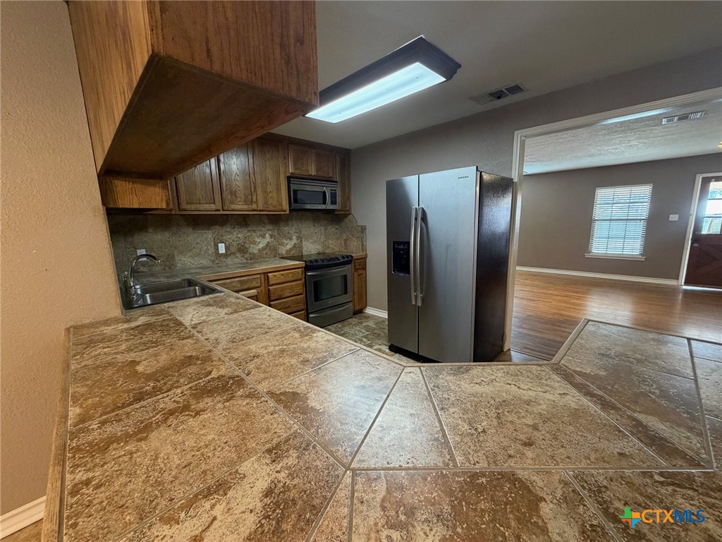 127 Hillcrest Drive Luling, TX 78648 - Photo 12 of 26 a kitchen with stainless steel appliances granite countertop a refrigerator a stove and a sink with wooden floor