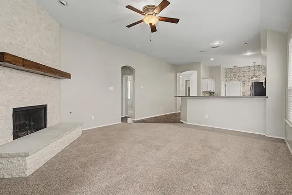 a view of a livingroom with a fireplace a ceiling fan and kitchen view