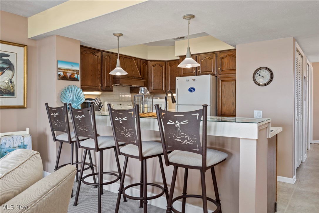 1507 Cleveland Road East, Unit 435 Huron, OH 44839 - Photo 10 of 37 Kitchen with custom exhaust hood, white refrigerator, hanging light fixtures, a breakfast bar, and decorative backsplash