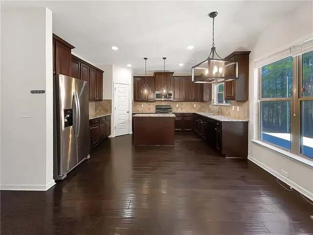 a kitchen with stainless steel appliances granite countertop a refrigerator a sink dishwasher a stove and a wooden floor