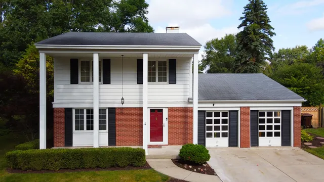 a view of a brick house with a yard plants and large tree