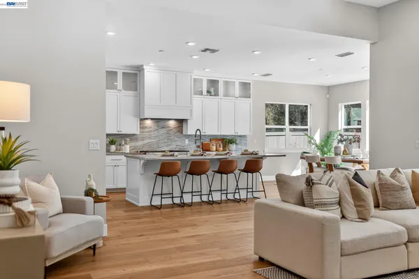 a kitchen with stainless steel appliances kitchen island granite countertop a refrigerator a stove a dining table and chairs with wooden floor