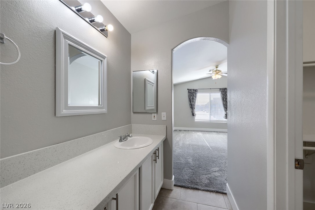 5985 High Steed Street, Unit 101 Henderson, NV 89011 - Photo 20 of 38 A well-appointed bathroom vanity with sleek white countertops and cabinetry, adjoined by an archway leading to a carpeted room with vaulted ceilings.