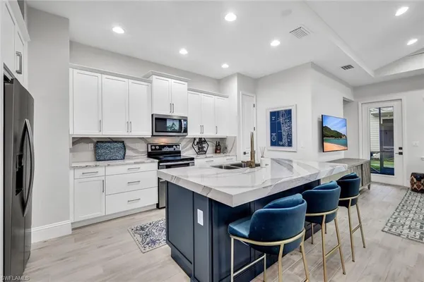 a kitchen with stainless steel appliances kitchen island granite countertop a sink a stove a refrigerator and white cabinets with wooden floor