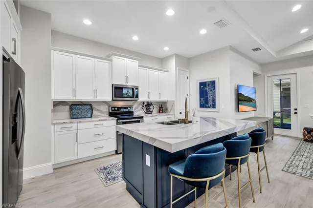 a kitchen with stainless steel appliances kitchen island granite countertop a sink a stove a refrigerator and white cabinets with wooden floor