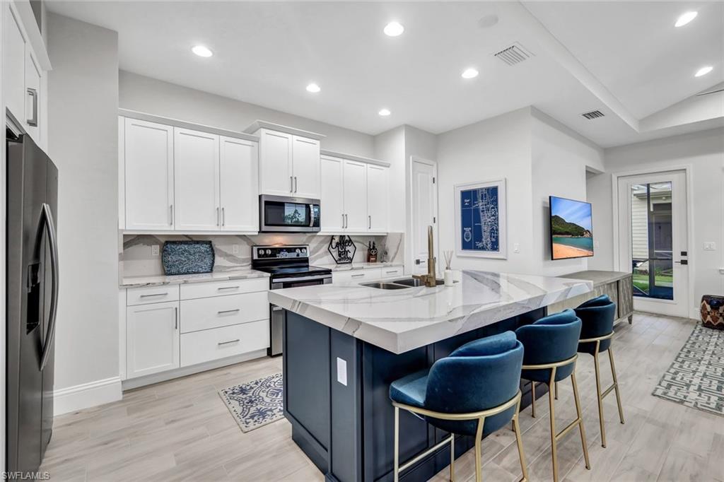 7142 Cayo Coco Lane Naples, FL 34113 - Photo 7 of 17 a kitchen with stainless steel appliances kitchen island granite countertop a sink a stove a refrigerator and white cabinets with wooden floor