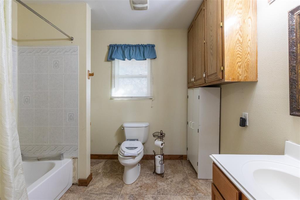 640 Ground Street Moran, TX 76464 - Photo 22 of 35 Bathroom featuring a white tub with tiled surround, a toilet, an opaque window, a vanity with an integrated sink, and wood-finish cabinetry