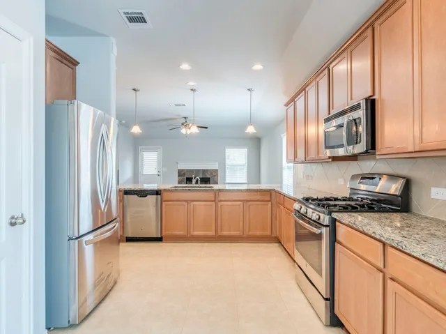 a large kitchen with stainless steel appliances granite countertop a refrigerator a sink dishwasher a stove and white cabinets with wooden floor