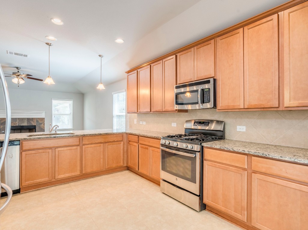 225 Razzmatazz Trail Buda, TX 78610 - Photo 6 of 28 a kitchen with stainless steel appliances granite countertop a stove top oven a sink dishwasher and a microwave oven with large trees