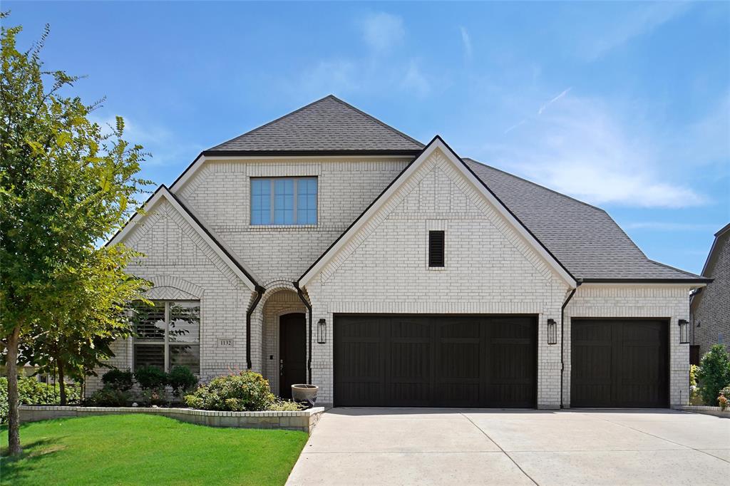 French country style house featuring driveway, brick siding, roof with shingles, a front lawn, and a garage