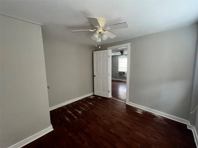 a view of an empty room with wooden floor and a ceiling fan