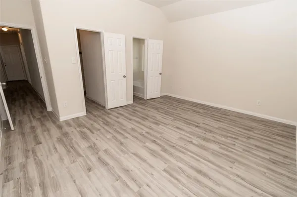 a view of an empty room with wooden floor and a bathroom