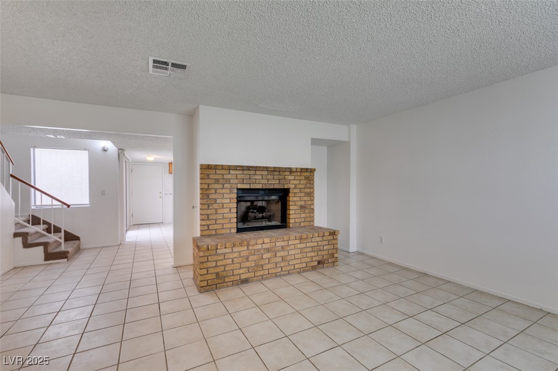 2681 Ruthe Duarte Avenue Las Vegas, NV 89121 - Photo 4 of 43 Unfurnished living room featuring visible vents, a brick fireplace, a textured ceiling, stairway, and light tile patterned flooring