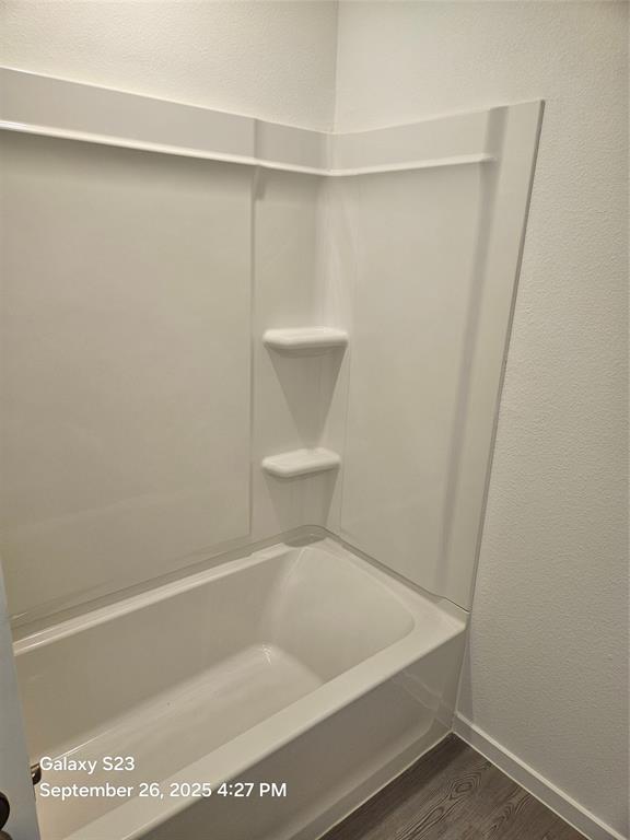 1021 Raintree Road Princeton, TX 75407 - Photo 13 of 16 Full bath featuring a textured wall, dark wood-style floors, and bathtub / shower combination