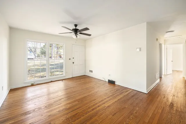 an empty room with wooden floor chandelier fan and windows