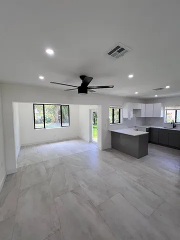 a view of an empty room with kitchen and window