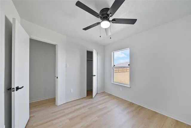 an empty room with wooden floor ceiling fan and windows