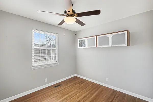 an empty room with wooden floor fan and windows