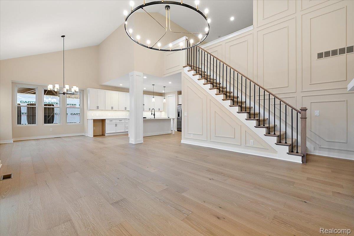 2044 Breckenridge Court Rochester, MI 48309 - Photo 15 of 33 Unfurnished living room featuring a chandelier, high vaulted ceiling, stairway, light wood-style floors, and a decorative wall