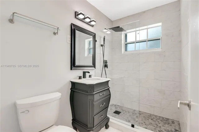 a bathroom with a toilet a sink a mirror a shower and vanity