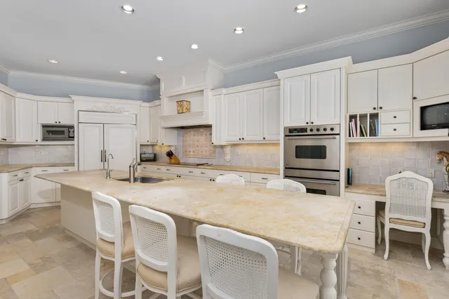 a kitchen with stainless steel appliances a stove top oven a refrigerator a sink and white cabinets with wooden chairs