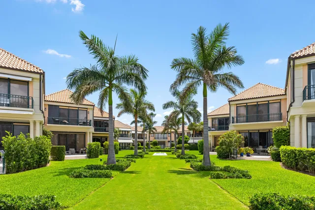 a view of a white house with a swimming pool and a big yard with palm trees