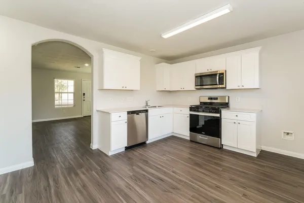 a kitchen with granite countertop a stove top oven a sink dishwasher and a refrigerator with wooden floor