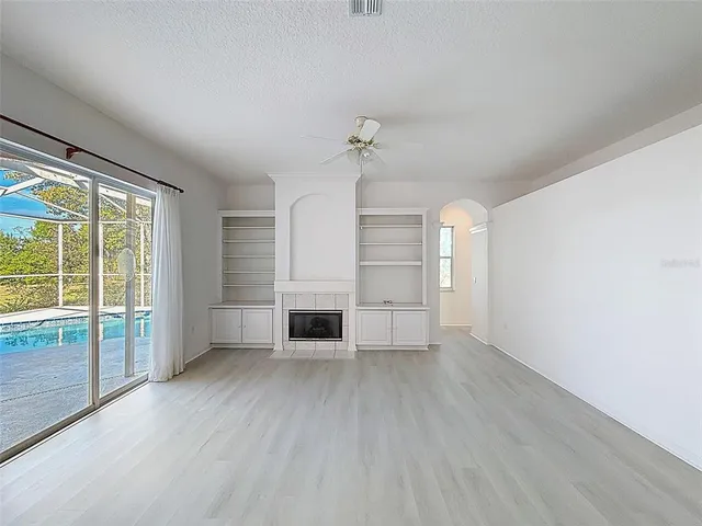 an empty room with wooden floor ceiling fan and windows