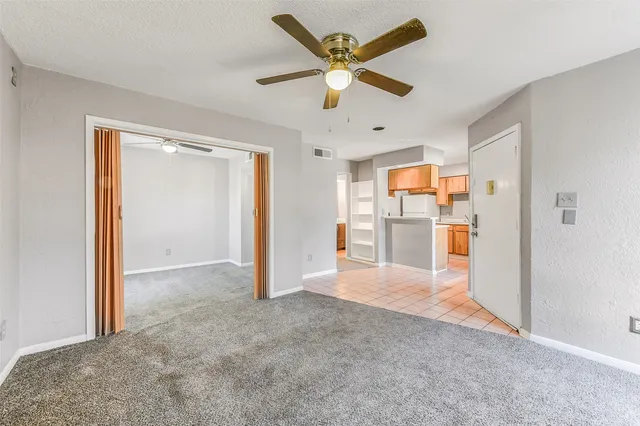 a view of a livingroom with a ceiling fan & kitchen space