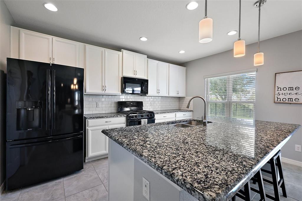 1292 Cavender Creek Road Minneola, FL 34715 - Photo 12 of 36 a kitchen with kitchen island granite countertop a refrigerator a stove a sink a counter space and cabinets