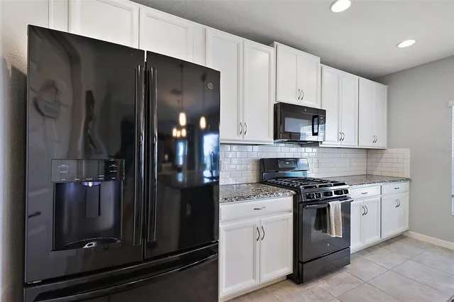 a kitchen with stainless steel appliances granite countertop a refrigerator a stove a sink and white cabinets