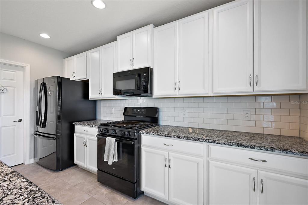 1292 Cavender Creek Road Minneola, FL 34715 - Photo 14 of 36 a kitchen with stainless steel appliances granite countertop a refrigerator a stove a sink and white cabinets
