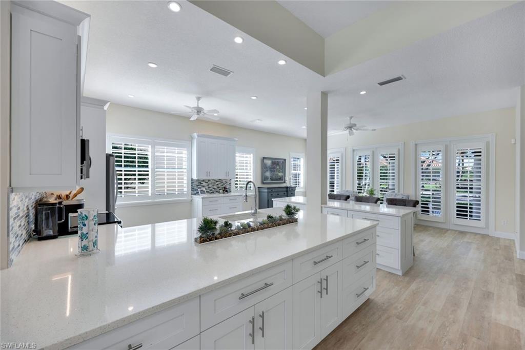 3108 Dominica Way Naples, FL 34119 - Photo 5 of 39 Expansive fully remodeled kitchen featuring a large island with a light-colored countertop, white shaker-style cabinetry with chrome hardware, and a mosaic tile backsplash