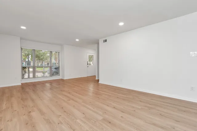 a view of an empty room with wooden floor and a window
